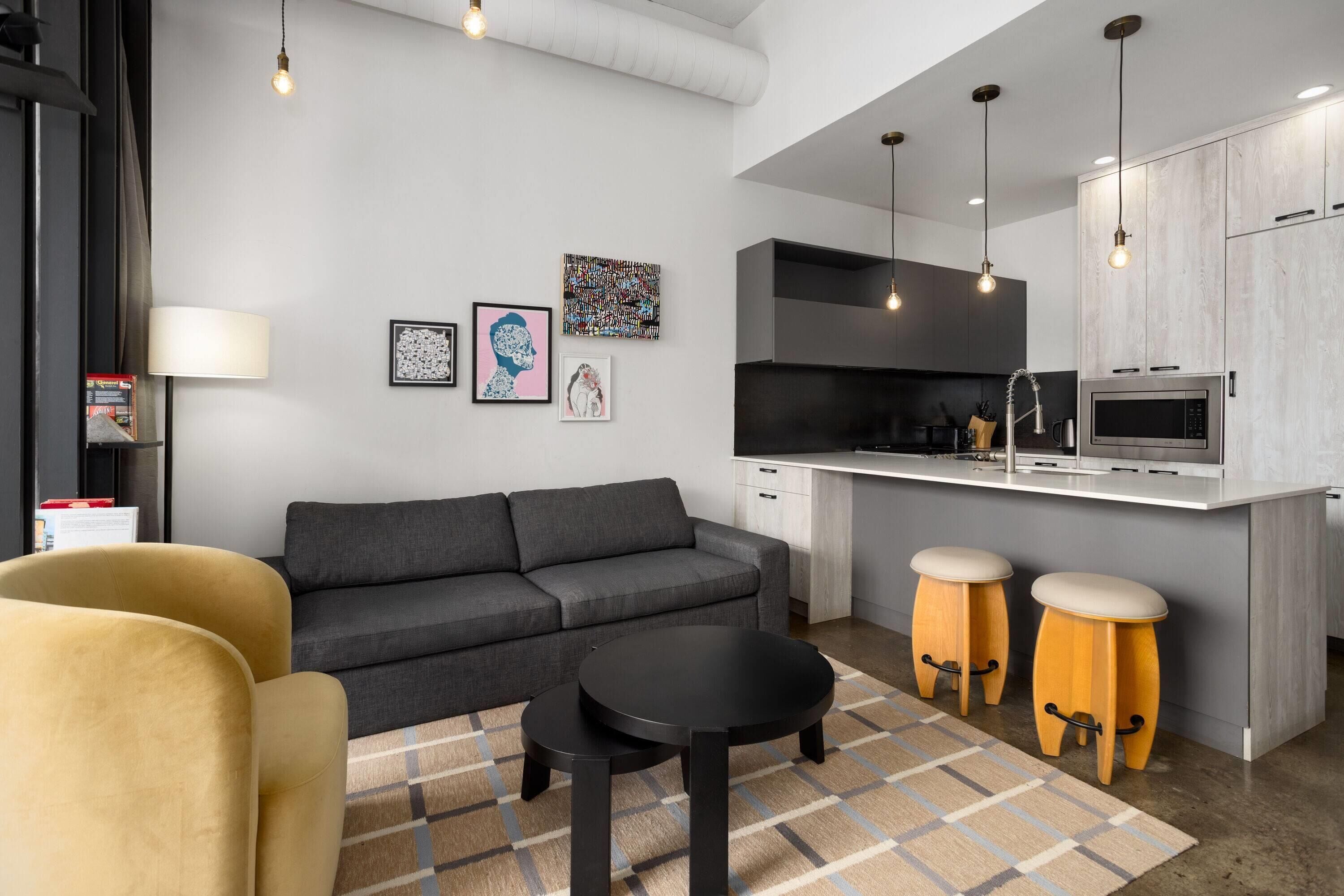 A modern living room with a sofa, two black tables, and wooden stools.
