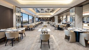 Un vaste espace de restauration d’hôtel, doté de nombreuses tables et chaises, de grandes fenêtres et d’un design moderne au niveau du plafond.