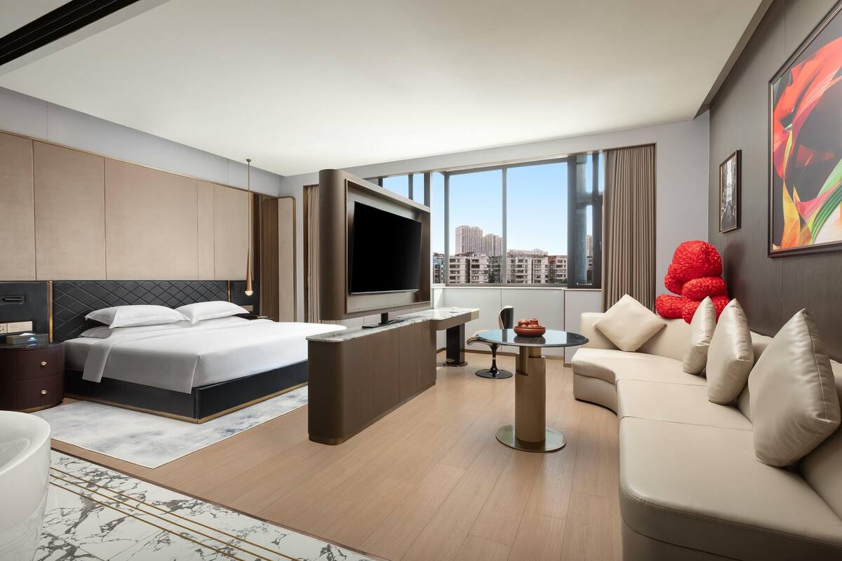 Una habitación de hotel moderna con una cama grande, un televisor, un sofá y un comedor.