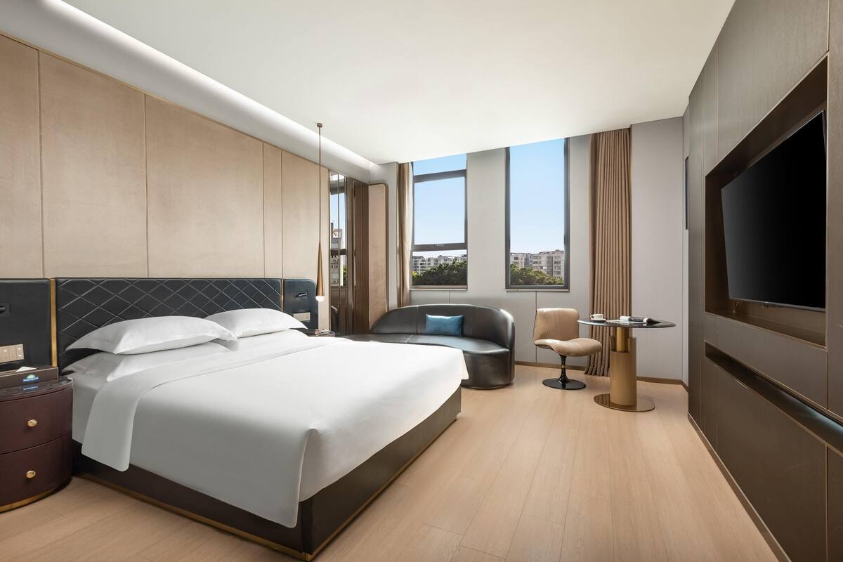 Una habitación de hotel moderna con una cama grande, un sofá, un televisor y vistas a la ciudad.