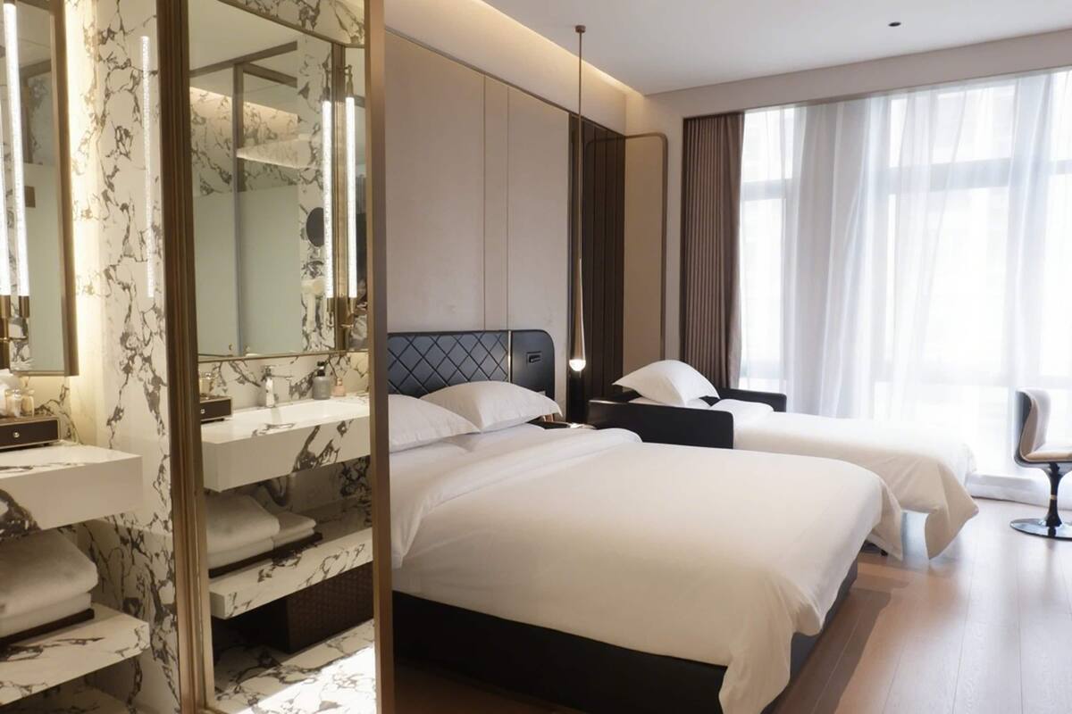 Habitación de hotel con dos camas, un espejo grande, una tocador con salpicadero de mármol y un ventanal con cortinas.