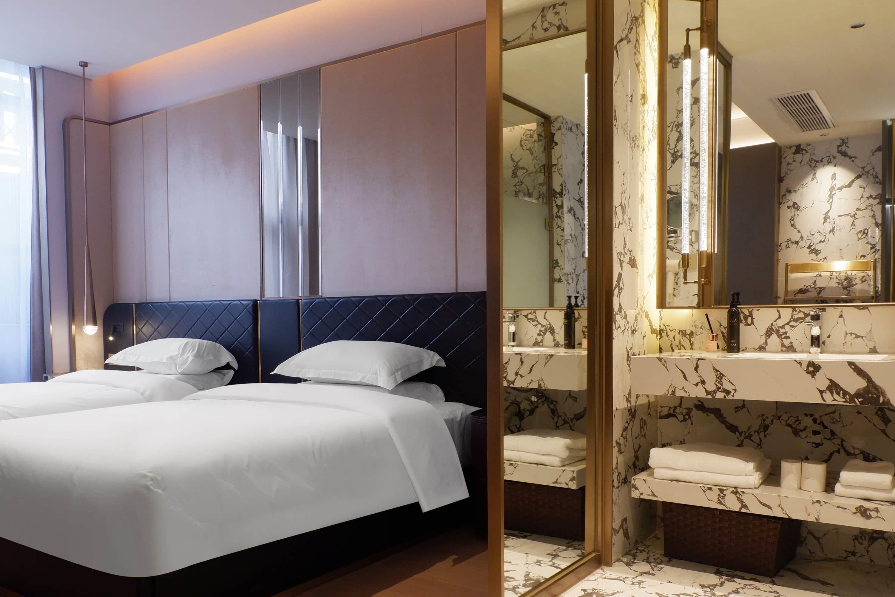 Una habitación de hotel con una cama grande, un baño independiente con tocador de mármol y un espejo.