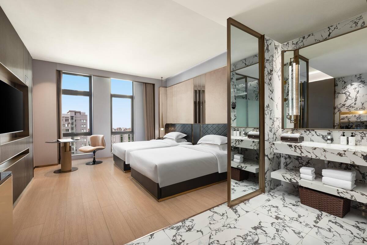 Una habitación de hotel moderna con dos camas, un espejo grande, un televisor y vista a la ciudad.