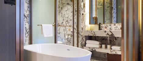 A modern bathroom with a freestanding bathtub, marble-patterned walls, a large mirror, and a vanity with towels.