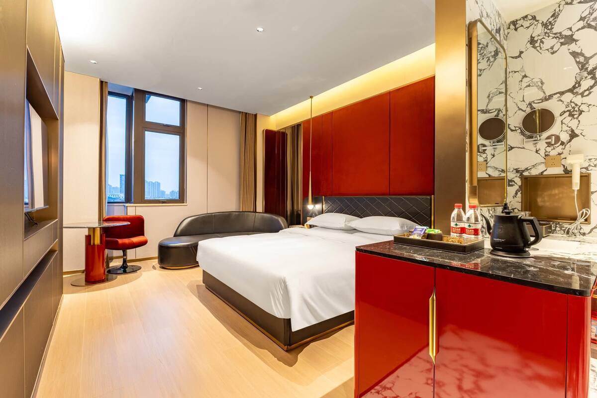 Una habitación de hotel moderna con una cama grande, un escritorio con cafetera y vistas a la ciudad a través de amplios ventanales.