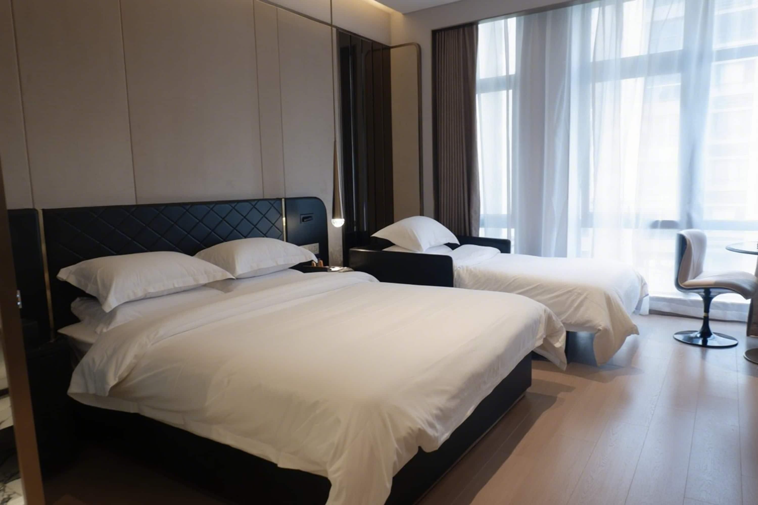 A hotel room with two beds, a chair, and a large window with curtains.