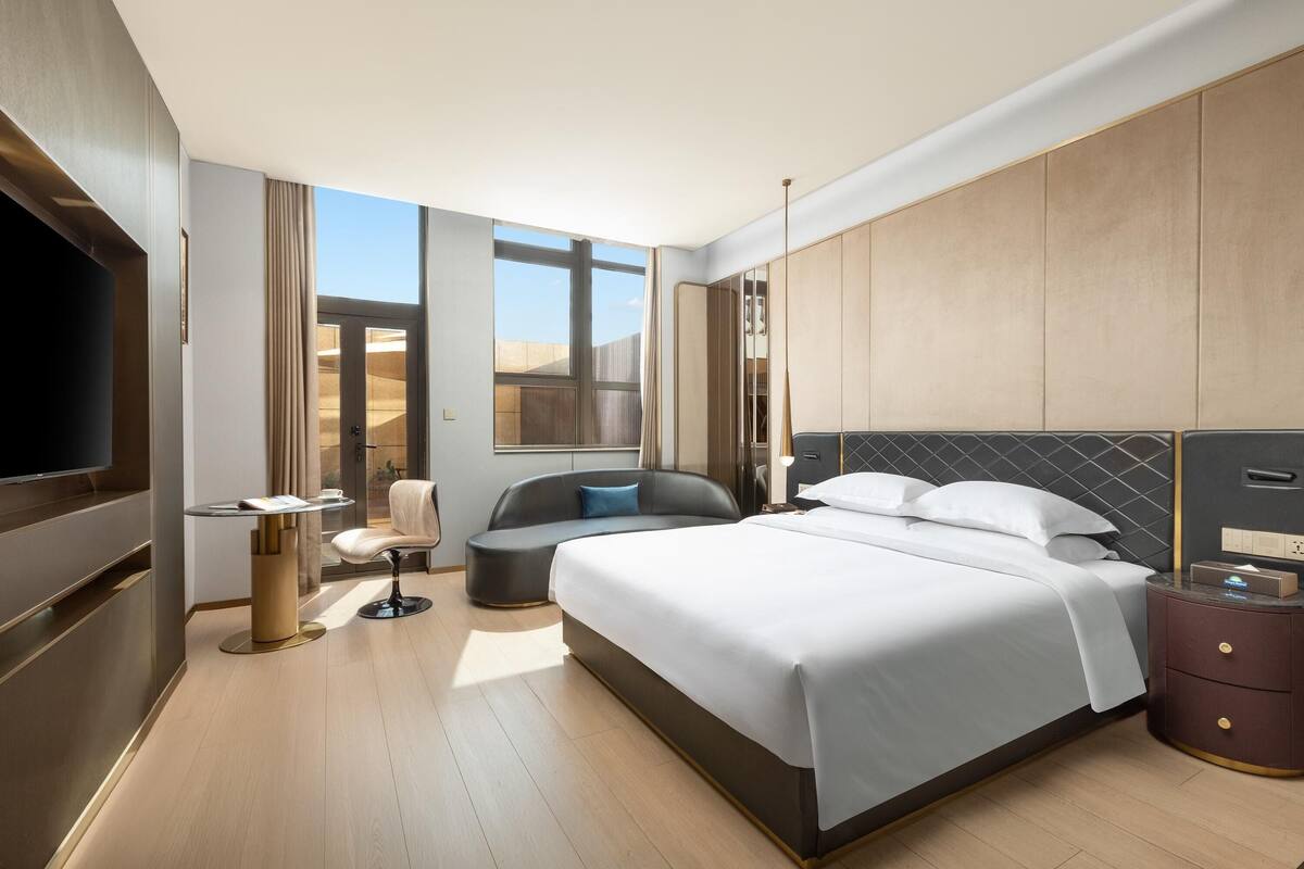 Habitación de hotel moderna con una cama grande, una zona de estar, televisión y vistas al desierto.