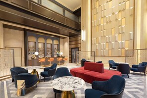 Eine geräumige Lobby mit einer roten Couch, mehreren Sesseln, einem Marmortisch und einer Rezeption mit Barbereich.