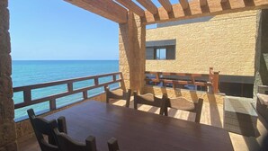 A wooden table and chairs in a room with a stone wall and a view of the sea.