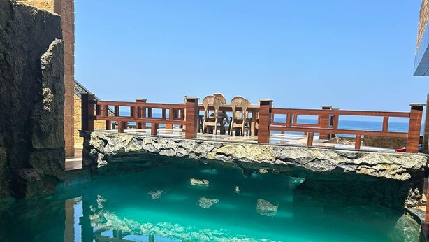 A clear pool with a wooden deck and stone walls, overlooking a body of water.