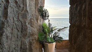 A narrow corridor with a view of the sea, a potted plant, and stone walls.