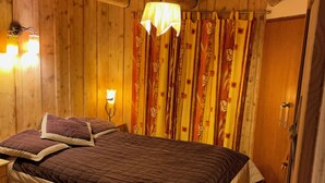 Dormitorio de cabaña de madera con una cama individual y una cama más pequeña, paredes de madera, una lámpara colgante y una puerta con manija.