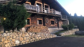Una cabaña de madera con balcón, cimientos de piedra y una pila de leña.