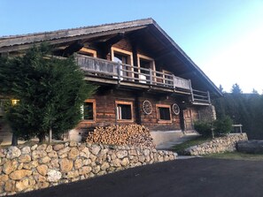 A wooden chalet with a balcony, stone foundation, and a stack of firewood. - Chalet for 10 people Crest Voland ski in ski out Large space Individual chalet (Crest-Voland)
