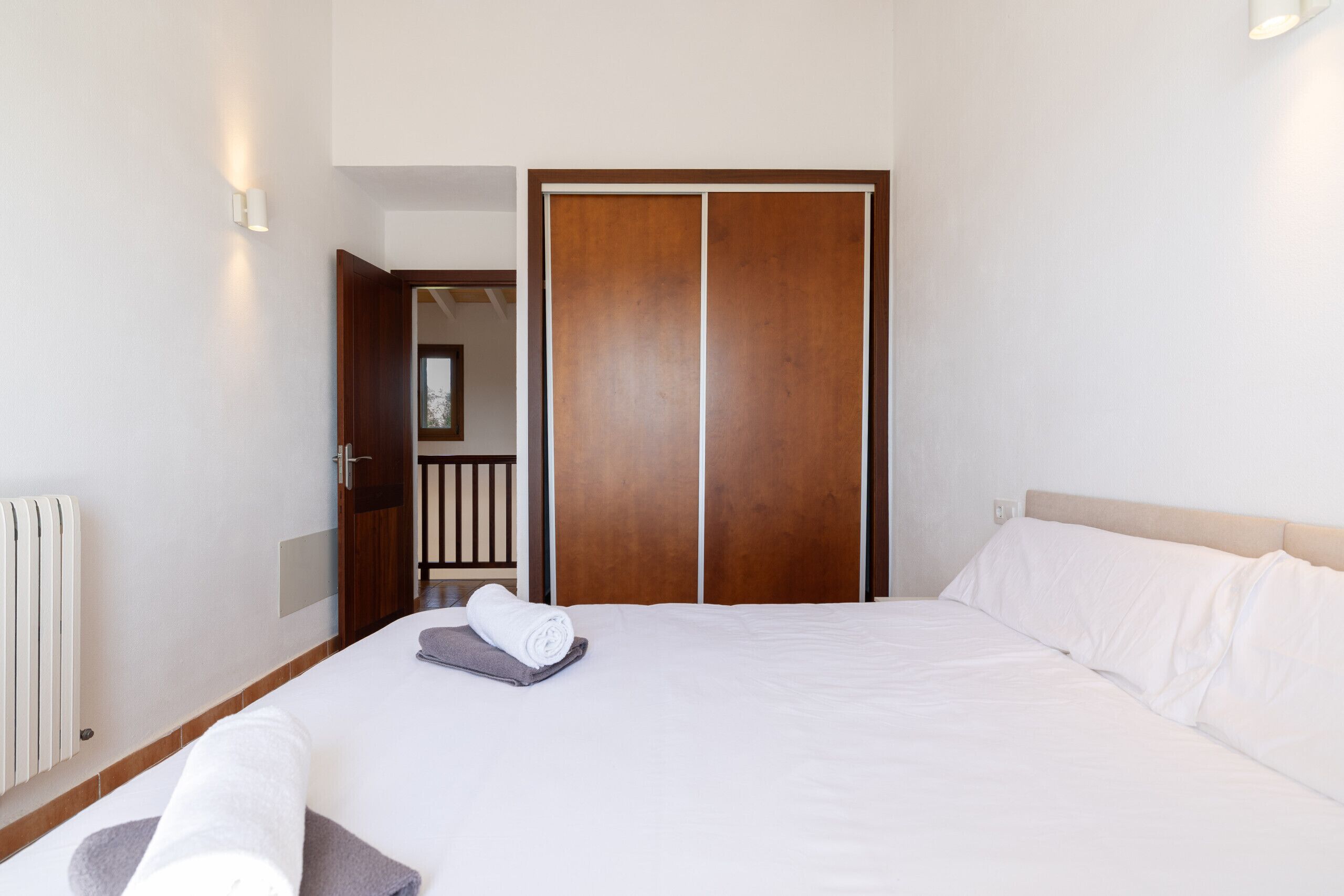 A hotel room with a bed, a wooden wardrobe, a radiator, and a wall-mounted light fixture.