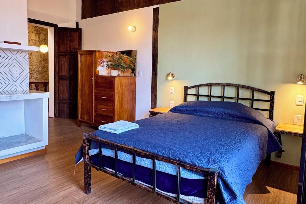 A bedroom with a wooden bed frame, a white bedside table, a wardrobe, and a hanging light fixture.