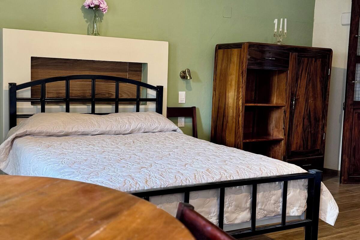 A room with a bed, a wooden table, a vase with flowers, and a wooden wardrobe.