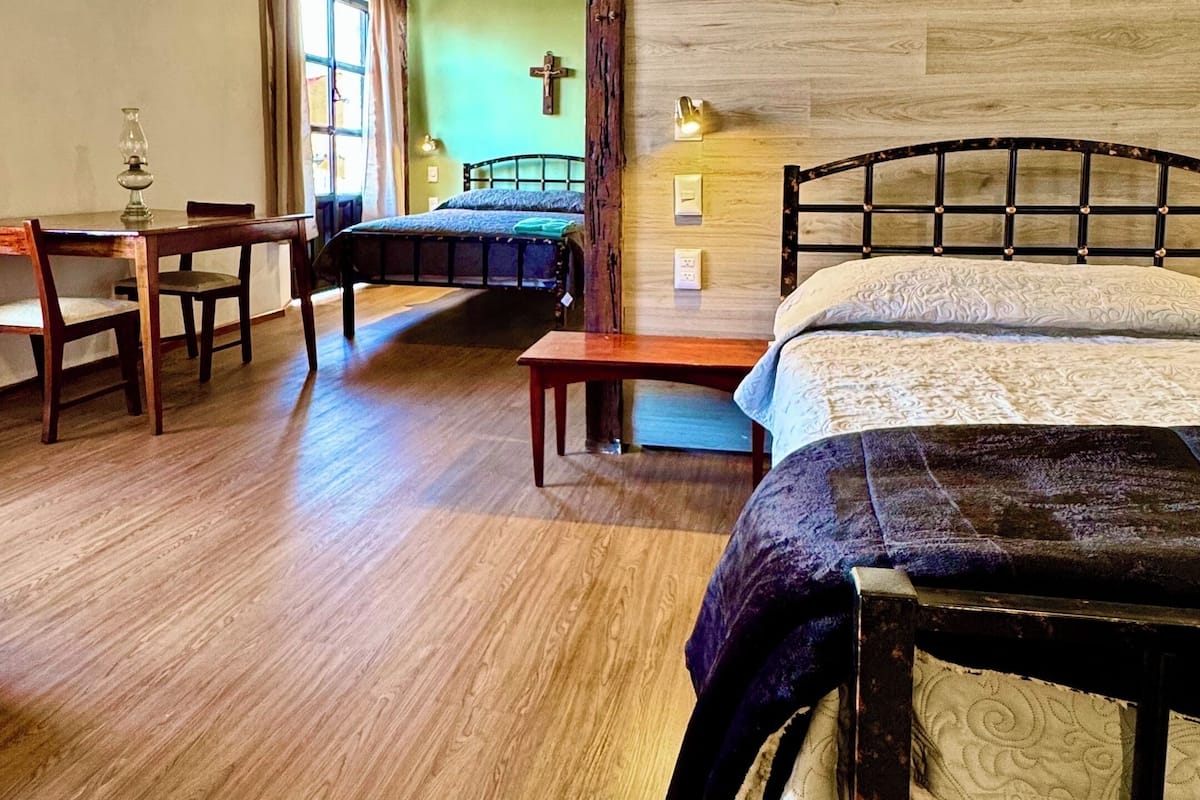 A rustic room with a wooden ceiling, a bed with a patterned bedspread, a wooden table with chairs, and a bench.