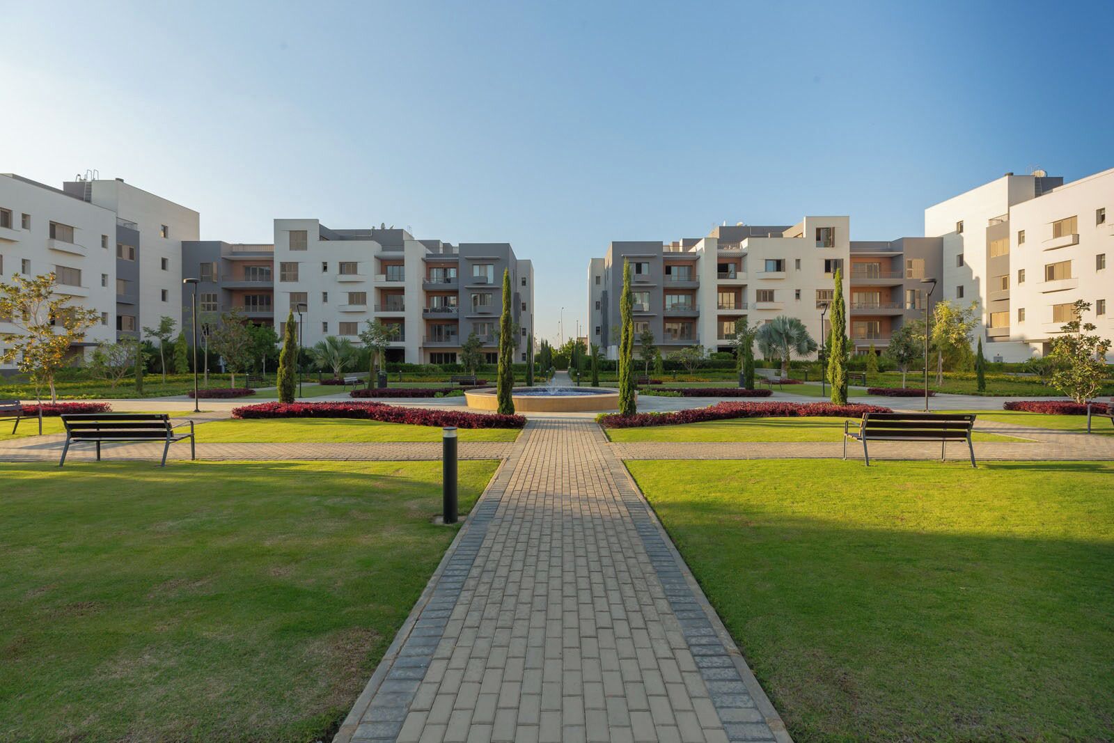 Un complesso residenziale moderno con un viale centrale, prati verdi e panchine.