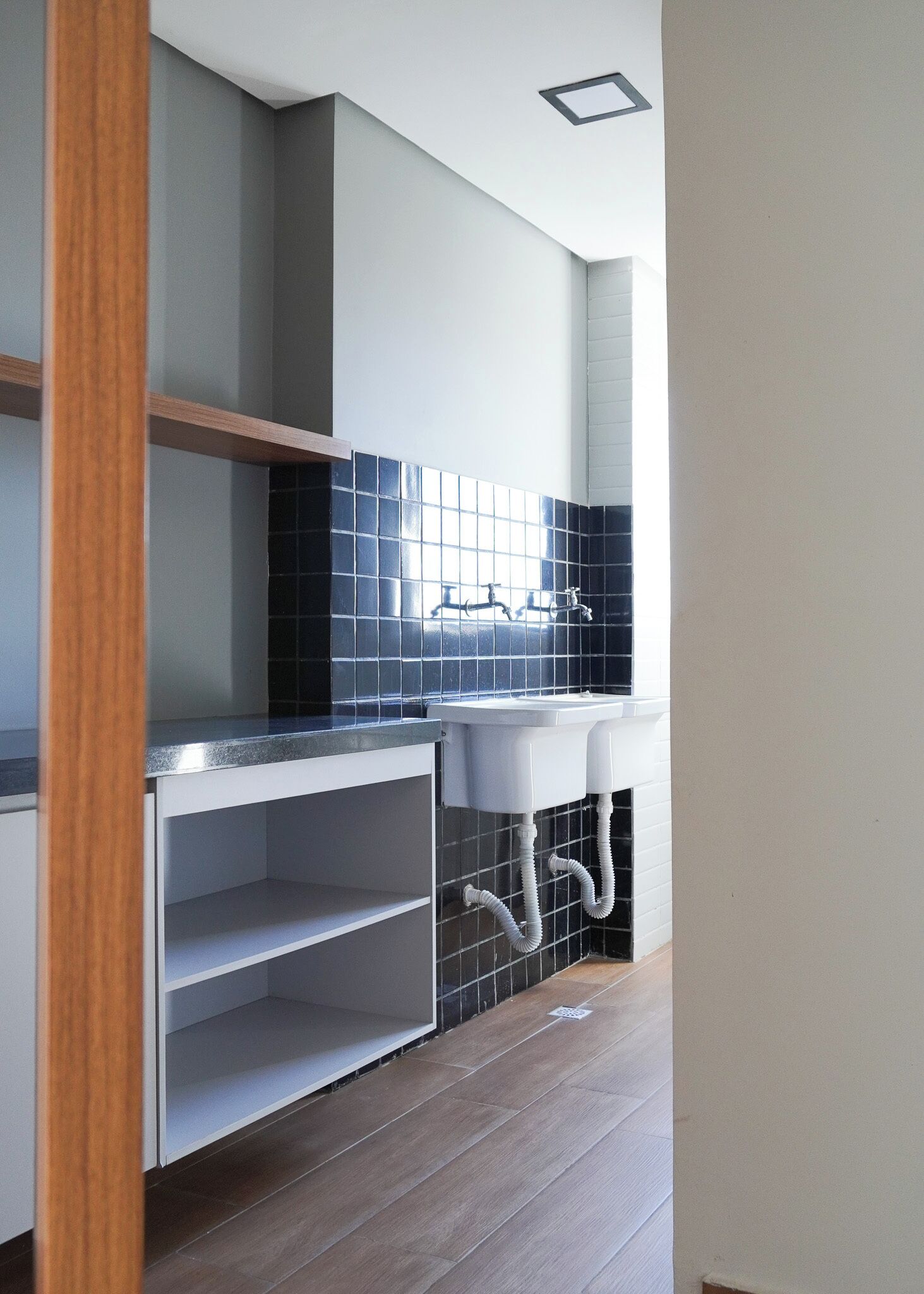 Una cucina moderna con un piano di lavoro bianco, una parete di fondo nera e un lavandino bianco.