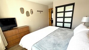 Een slaapkamer met een bed, een televisie op een houten dressoir, een deur met geëtste glaspanelen en een kapstok aan de muur.
