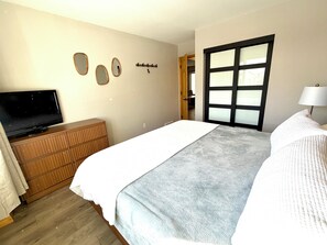A bedroom with a bed, a television on a wooden dresser, a door with frosted glass panels, and a wall-mounted coat rack. - Cozy Family 2-Bedroom Getaway in Canmore,  perfect for families! (Canmore)