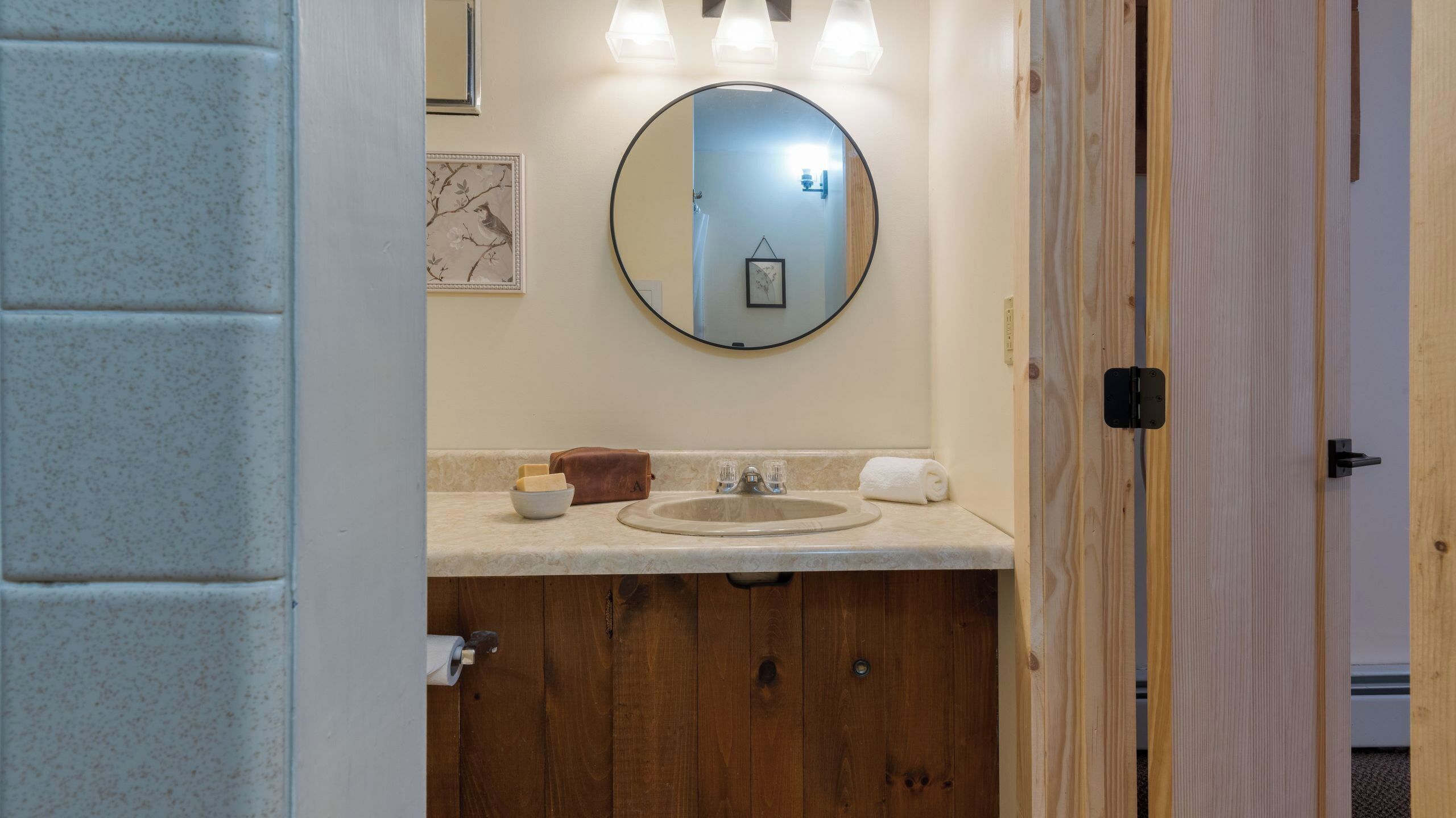 A bathroom with a wooden vanity, a round mirror, and a sink.