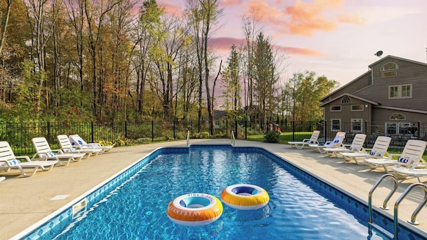 A swimming pool with lounge chairs and inflatable rings, surrounded by trees and a building. - Sleeps 40 Heated Pool Hot Tub Fire Pit Game Room Brookside Mountain Retreat by Avantstay (Stephentown)