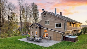 A two-story house with a patio area, a hot tub, and a play structure in the yard. - Sleeps 40 Heated Pool Hot Tub Fire Pit Game Room Brookside Mountain Retreat by Avantstay (Stephentown)