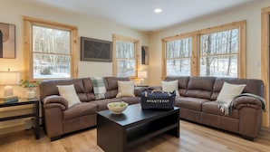 A cozy living room with two brown leather sofas, a black coffee table, and large windows offering a view of a snowy forest. - Sleeps 40 Heated Pool Hot Tub Fire Pit Game Room Brookside Mountain Retreat by Avantstay (Stephentown)