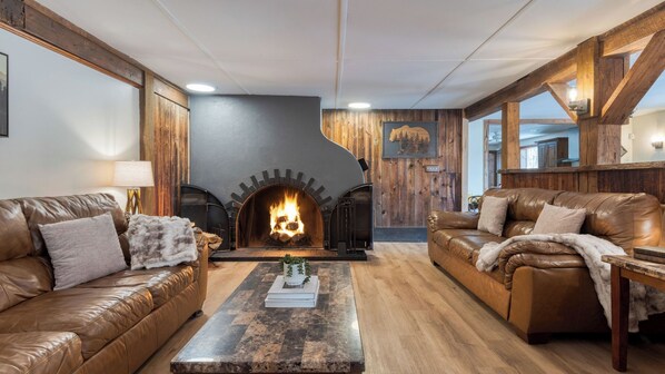 A cozy living room with a fireplace, leather sofas, and wooden walls. - Sleeps 40 Heated Pool Hot Tub Fire Pit Game Room Brookside Mountain Retreat by Avantstay (Stephentown)