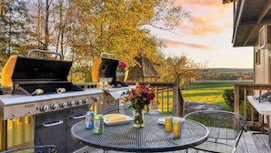 A barbecue grill with multiple burners, a table with drinks and food, and a scenic view of trees and a house. - Sleeps 40 Heated Pool Hot Tub Fire Pit Game Room Brookside Mountain Retreat by Avantstay (Stephentown)