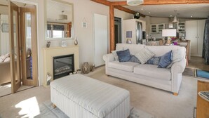 A spacious living room with a fireplace, a sofa, and a dining area in the background. - 1 Fishermans Hill (Newton Stewart)