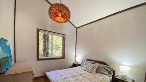 Ein Schlafzimmer mit Bett, Fenster, Nachttisch und einer Pendelleuchte.