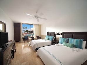 Une chambre d’hôtel avec deux lits, un bureau avec une télévision, une chaise, une vue sur la piscine et un ventilateur de plafond.