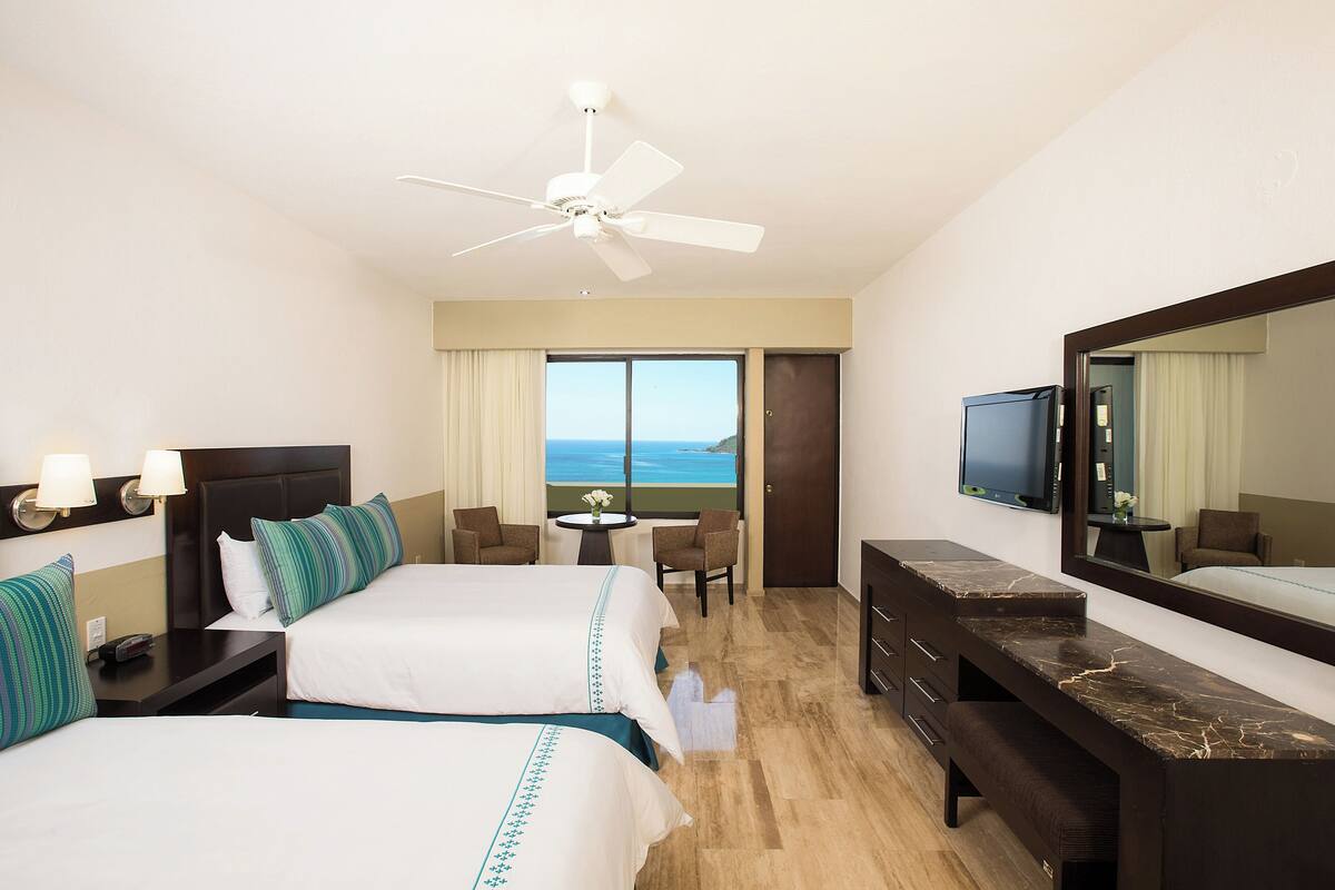 Une chambre d’hôtel avec deux lits, un bureau, une chaise, une télévision et une grande fenêtre donnant sur un beau paysage.