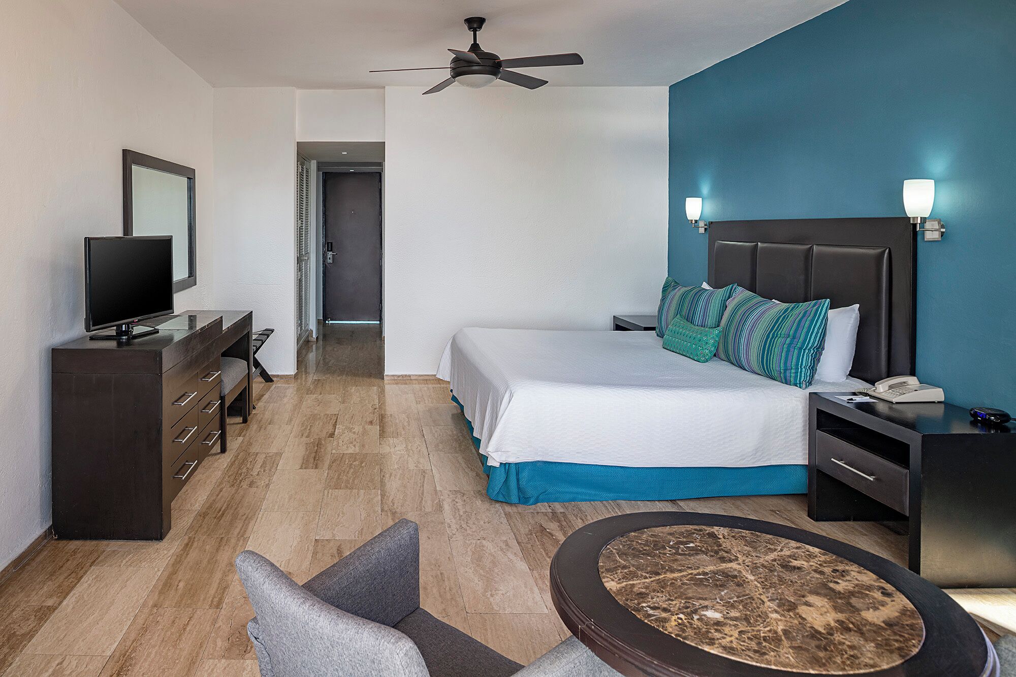Une chambre d’hôtel équipée d’un lit, d’une table de chevet, d’un bureau, d’une télévision et d’un ventilateur de plafond.
