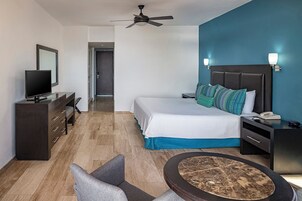 Habitación de hotel con cama, mesita de noche, escritorio, televisor y ventilador de techo.
