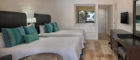 A hotel room with two beds, a desk, a chair, a round table, a ceiling fan, and a TV mounted on the wall.