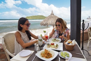 Dos personas cenando en una mesa al aire libre con vista al océano y a la playa.
