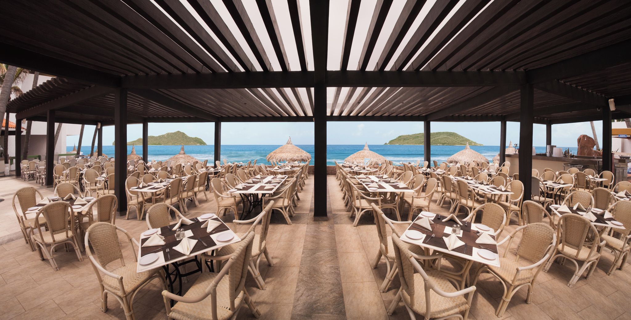 An outdoor dining area with tables and chairs, overlooking the sea.