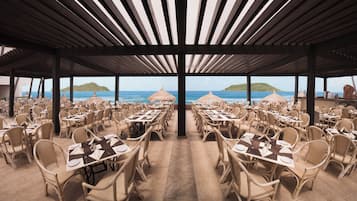An outdoor dining area with tables and chairs, overlooking the sea.