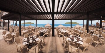 Un área de comedor al aire libre con mesas y sillas, con vista al mar.