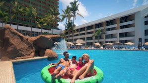 A swimming pool with a rock feature and palm trees, surrounded by a hotel building with multiple balconies. - El Cid Castilla Beach Hotel - All Inclusive (Mazatlán)