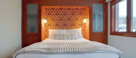A hotel room with a large bed, two bedside lamps, a patterned wallpaper headboard, and a window with a view.