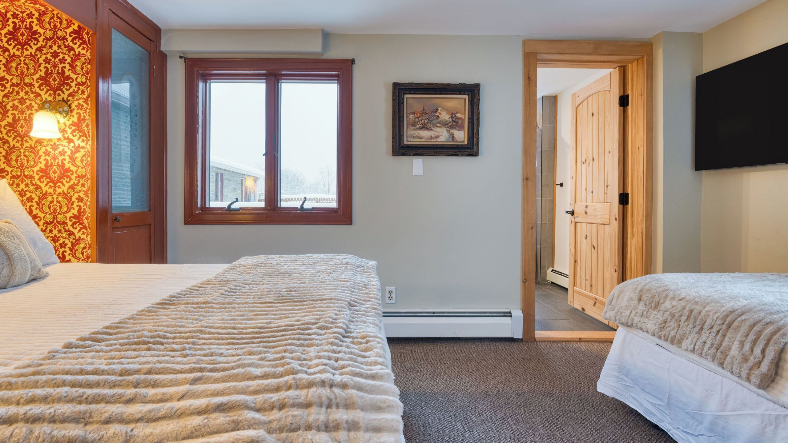A hotel room with two beds, a large window, a painting on the wall, and a wooden door.