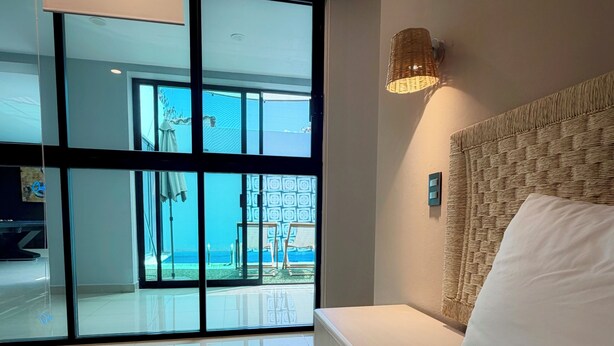 Un dormitorio con una cama grande, vistas a un área exterior por una puerta corrediza de vidrio y una lámpara fijada a la pared.