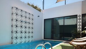 Una piscina con un diseño geométrico en la pared, puerta de entrada de vidrio y un área de estar cubierta.