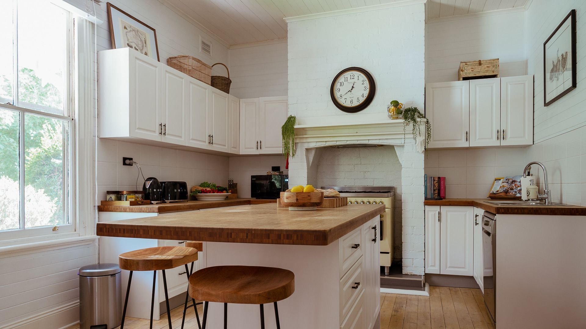 A kitchen with white cabinetry, a wooden island, a clock on the wall, and a window providing natural light.
