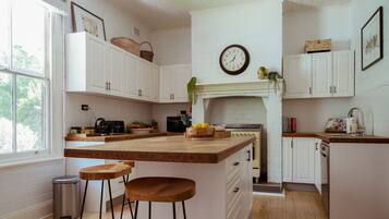 A kitchen with white cabinetry, a wooden island, a clock on the wall, and a window providing natural light.